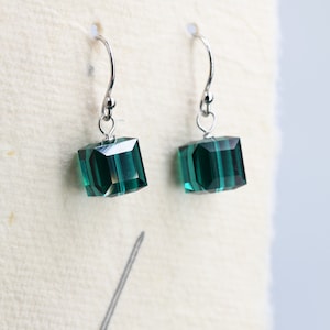 May include: A pair of silver earrings with dark green square-shaped crystal drops.