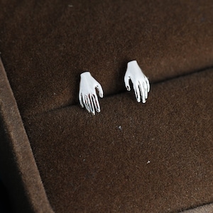 May include: A pair of silver hand-shaped stud earrings. The earrings are small and delicate, and they are perfect for adding a touch of whimsy to any outfit.