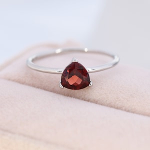 May include: A silver ring with a triangular red gemstone.