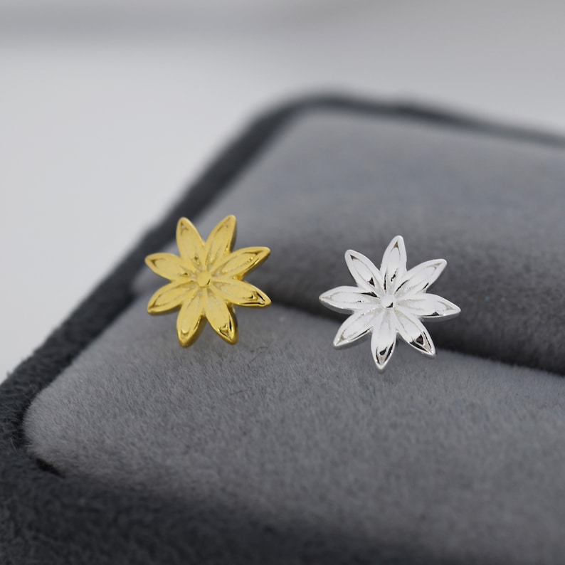 May include: A pair of flower-shaped earrings, one gold and one silver. The earrings are small and delicate, with a simple design.