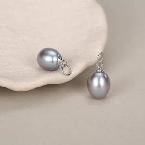 Peut inclure: Deux perles ovales gris irisé, chacune dotée d'une bélière en métal argenté poli et d'un petit anneau de jonction circulaire fixé sur le dessus, conçues pour être utilisées comme composants de bijoux ou pendentifs pour colliers.