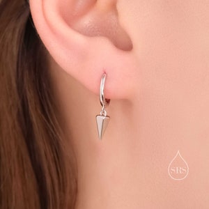 May include: Silver hoop earrings with a silver pyramid charm hanging from the bottom.