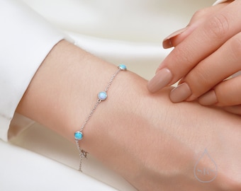 Peut inclure: Un bracelet délicat en argent avec quatre petites pierres rondes d'opale. Les pierres ont une couleur irisée bleu clair et blanc.