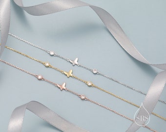 May include: Three delicate silver, gold, and rose gold butterfly charm bracelets with small clear cubic zirconia stones. The bracelets are displayed on a light blue background with a silver ribbon.