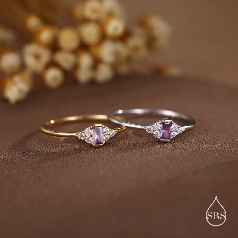 Puede incluir: Dos anillos delicados con una piedra preciosa p&uacute;rpura y peque&ntilde;as piedras transparentes. El anillo de la izquierda es de oro y el anillo de la derecha es de plata.