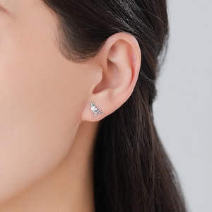 May include: Silver dove earrings with green gemstone accents. The dove is facing right and has its wings spread.