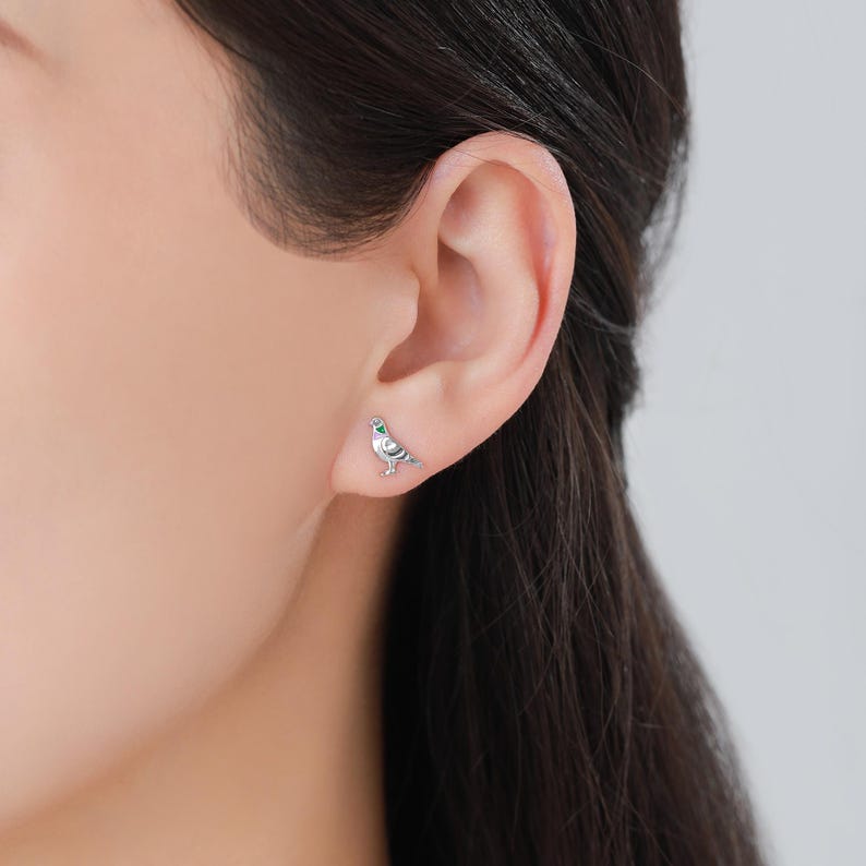 May include: Silver dove earrings with green gemstone accents. The dove is facing right and has its wings spread.