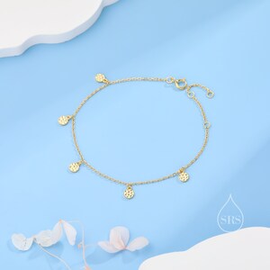 Puede incluir: Un brazalete de cadena dorada con cinco peque&ntilde;os colgantes redondos texturizados. El brazalete est&aacute; sobre un fondo azul claro.