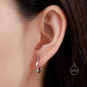 Może przedstawiać: Zbliżenie na ucho z srebrnym, skręconym kolczykiem w kształcie koła. Kolczyk jest prosty w designie i ma gładkie wykończenie.