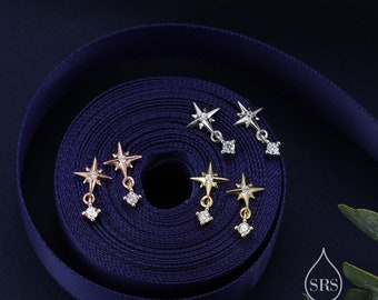 May include: Four pairs of star-shaped earrings with a dangling crystal. The earrings are displayed on a blue ribbon.