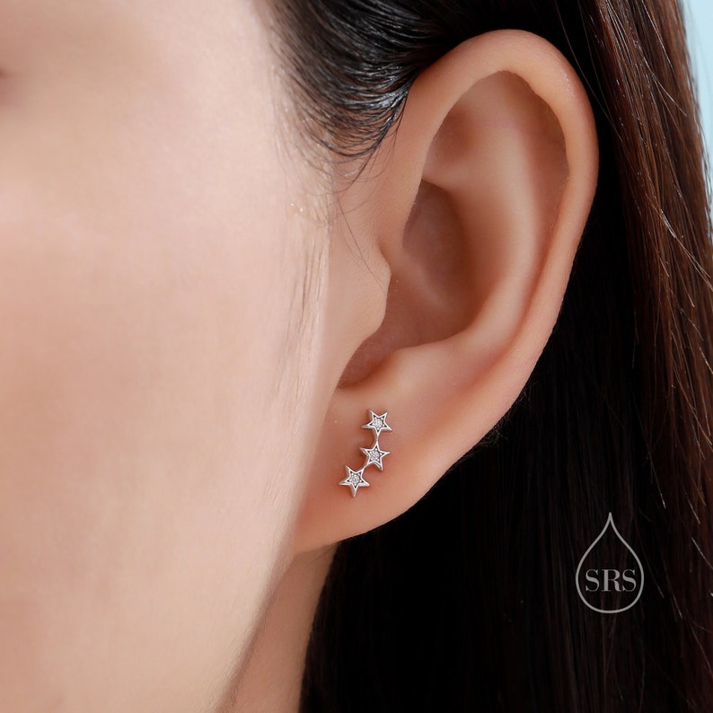 May include: Silver star stud earrings with small clear cubic zirconia stones. The earrings are arranged in a diagonal line, with the largest star at the top and the smallest star at the bottom.