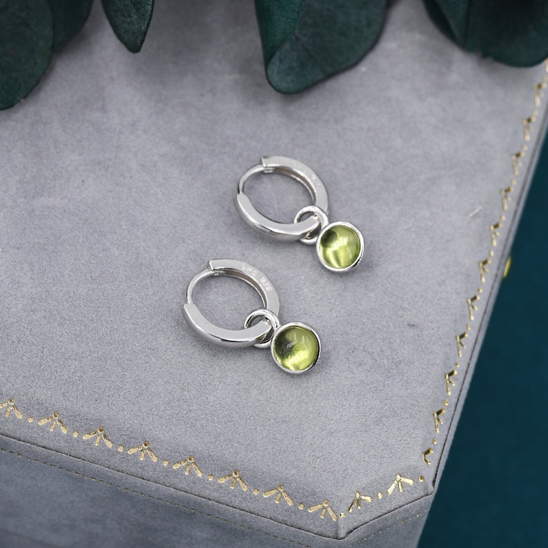 May include: A pair of silver hoop earrings with a small, round, light green gemstone dangling from each hoop.