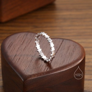 May include: A silver ring with a band of small star-shaped details. The ring is displayed on a wooden heart-shaped box.