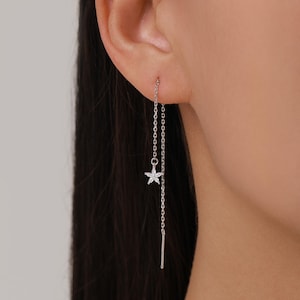 May include: A silver threader earring with a small, five-petal flower charm. The flower is adorned with small, clear gemstones. The earring hangs from a delicate chain and features a straight bar at the end.