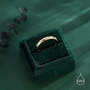 May include: A gold band ring with small diamonds set in a star pattern. The ring is displayed in a green velvet ring box.