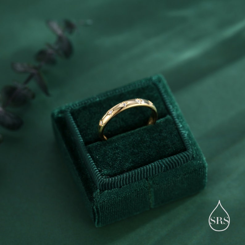 May include: A gold band ring with small diamonds set in a star pattern. The ring is displayed in a green velvet ring box.