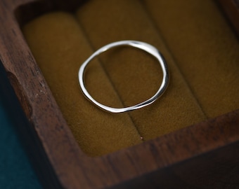 May include: A simple silver ring with a slightly irregular, hammered finish. The ring is displayed in a wooden box with a brown velvet lining.