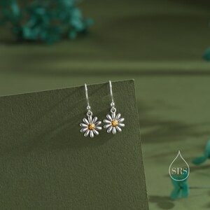 May include: A pair of silver dangle earrings with a daisy design. The center of the daisy is gold.