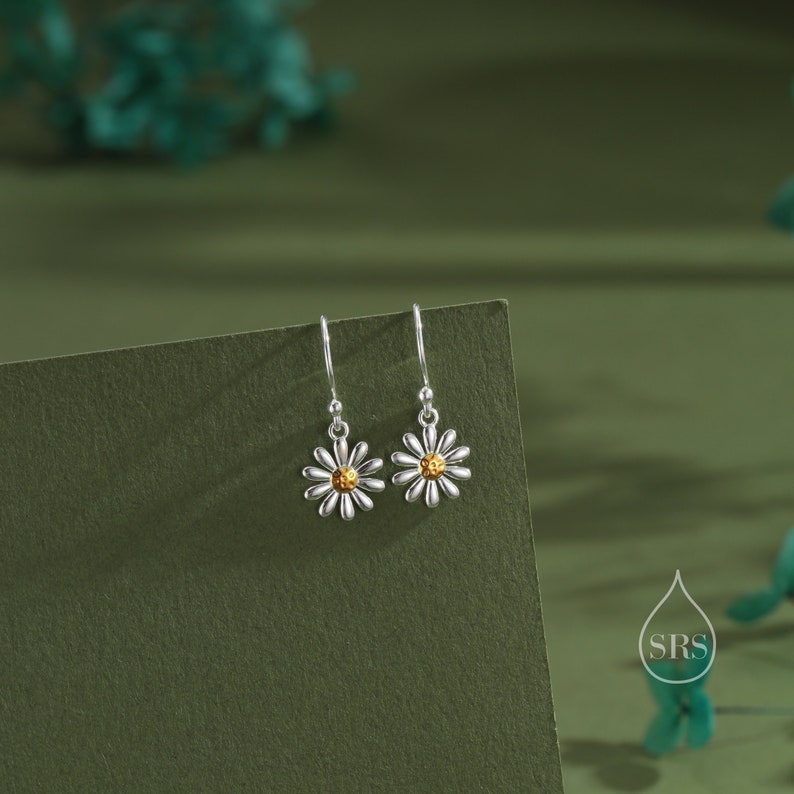 May include: A pair of silver dangle earrings with a daisy design. The center of the daisy is gold.
