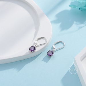 May include: A pair of silver dangle earrings with a small round purple gemstone hanging from each earring.