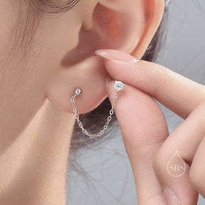 May include: A silver chain earring with a small clear stone at the top and a silver ball at the bottom.