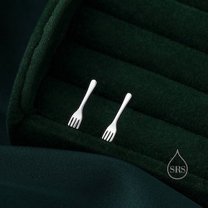 May include: A pair of silver fork-shaped earrings on a dark green velvet background.