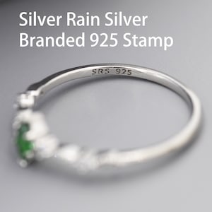 Puede incluir: Un anillo de plata con una piedra verde y peque&ntilde;as piedras transparentes. El anillo est&aacute; estampado con "SRS 925" en el interior.