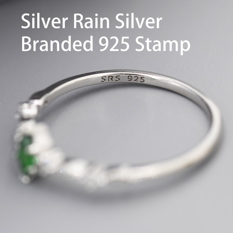 Puede incluir: Un anillo de plata con una piedra verde y peque&ntilde;as piedras transparentes. El anillo est&aacute; estampado con "SRS 925" en el interior.