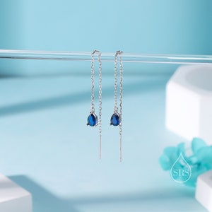Puede incluir: Un par de pendientes de plata con detalles de piedras preciosas azules. Los pendientes tienen un diseño delicado de cadena y una pequeña piedra preciosa en forma de lágrima al final de cada cadena.