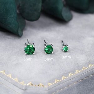 May include: Three silver stud earrings with green gemstones. The earrings are arranged in a row from largest to smallest, with the largest earring measuring 6mm, the middle earring measuring 5mm, and the smallest earring measuring 3mm.