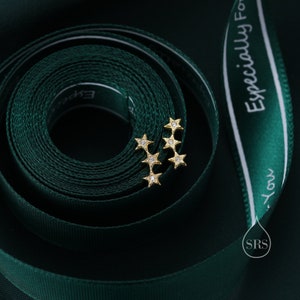 May include: Two gold star-shaped earrings with small clear stones set in each point of the star. The earrings are on a green ribbon with white text that reads "Especially For You".
