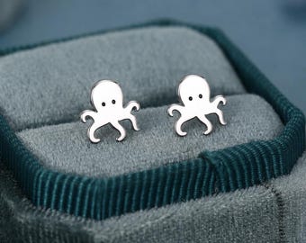 May include: A pair of silver-toned stud earrings shaped like small octopuses. Each earring features a smooth, polished surface with two tiny black dots representing eyes and multiple curved tentacles extending from the base of the head.