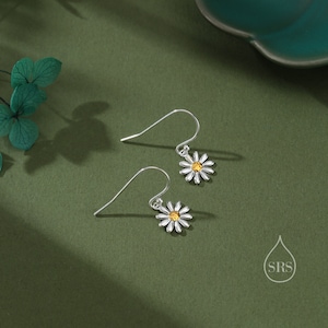 May include: A pair of silver dangle earrings with a white daisy flower charm and a yellow center stone.