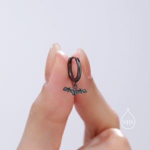 May include: Black hoop earring with a small bat charm hanging from it.