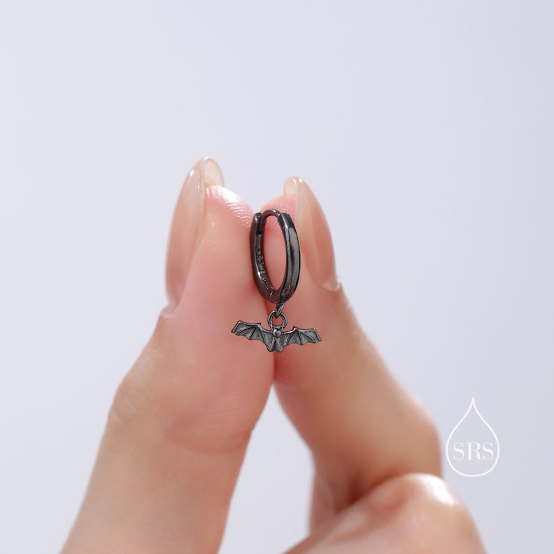 May include: Black hoop earring with a small bat charm hanging from it.