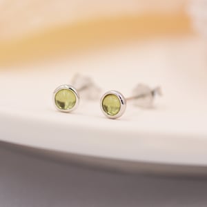 Puede incluir: Un par de pendientes de botón de plata con pequeñas piedras redondas de color verde claro.