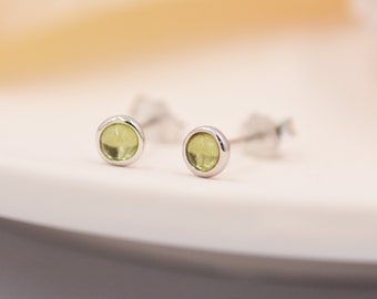 May include: A pair of silver stud earrings with small, round, light green gemstones.
