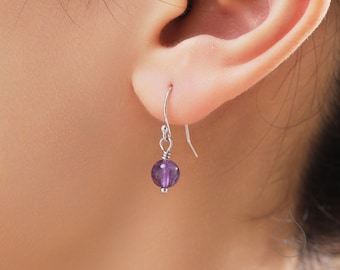 May include: A pair of silver dangle earrings with a single round purple amethyst gemstone on each earring.