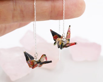 May include: A pair of silver dangle earrings with origami cranes made from black and colorful patterned paper. The cranes are suspended from the earrings by a silver chain.