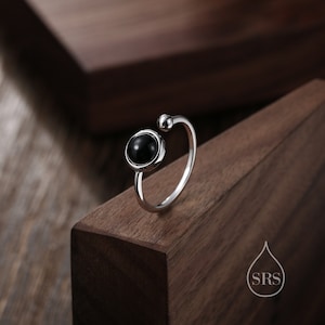 May include: A silver ring with a black stone set in a circular bezel. The ring has a simple, modern design and is perfect for everyday wear.