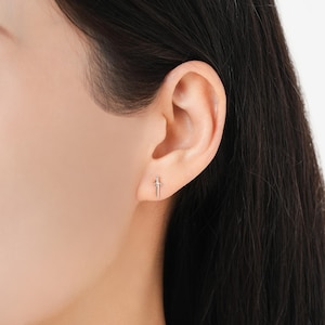 Peut inclure: Une boucle d'oreille en argent en forme de petite &eacute;p&eacute;e est port&eacute;e sur une oreille. La boucle d'oreille pr&eacute;sente un design d&eacute;taill&eacute; de la garde et de la lame. Le fond est de couleur claire, et l'accent est mis sur la boucle d'oreille.
