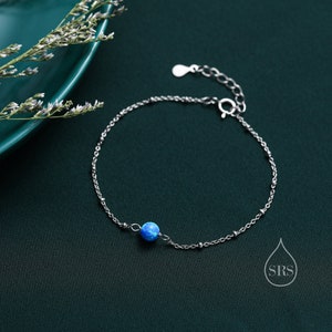 Op de afbeelding: Een delicate zilveren kettingarmband met een enkele blauwe opaal kraal. De armband heeft een karabijn sluiting.