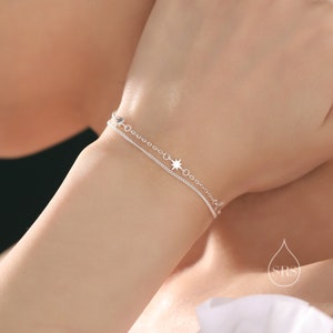 Può includere: Un braccialetto a catena d'argento con un delicato ciondolo a forma di stella. Il braccialetto è composto da due catene, una più spessa dell'altra.