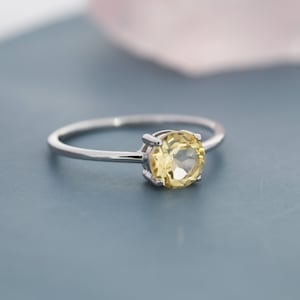Puede incluir: Un anillo de plata con una piedra preciosa amarilla. El anillo está sobre una superficie azul.