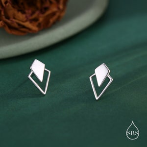 May include: A pair of silver geometric stud earrings with a diamond shape design. The earrings are on a green background.
