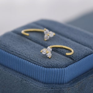 May include: A pair of gold hoop earrings with a cluster of three small, clear cubic zirconia stones on each earring.