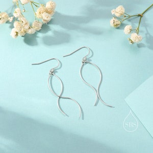 May include: A pair of silver dangle earrings with a twisted, wavy design. The earrings are on a light blue background.