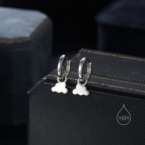 Puede incluir: Un par de pendientes de aro de plata con un pequeño dije en forma de nube que cuelga de cada aro.