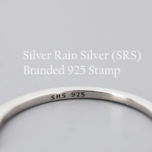 May include: Close-up of a silver ring with the inscription "SRS 925" on the inside band. The ring is a simple band style.
