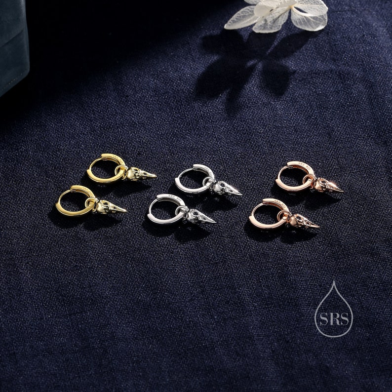 K&ouml;nnte beinhalten: Drei Paar Creolen mit einem Totenkopf-Anh&auml;nger. Die Ohrringe sind in Gold, Silber und Ros&eacute;gold erh&auml;ltlich.